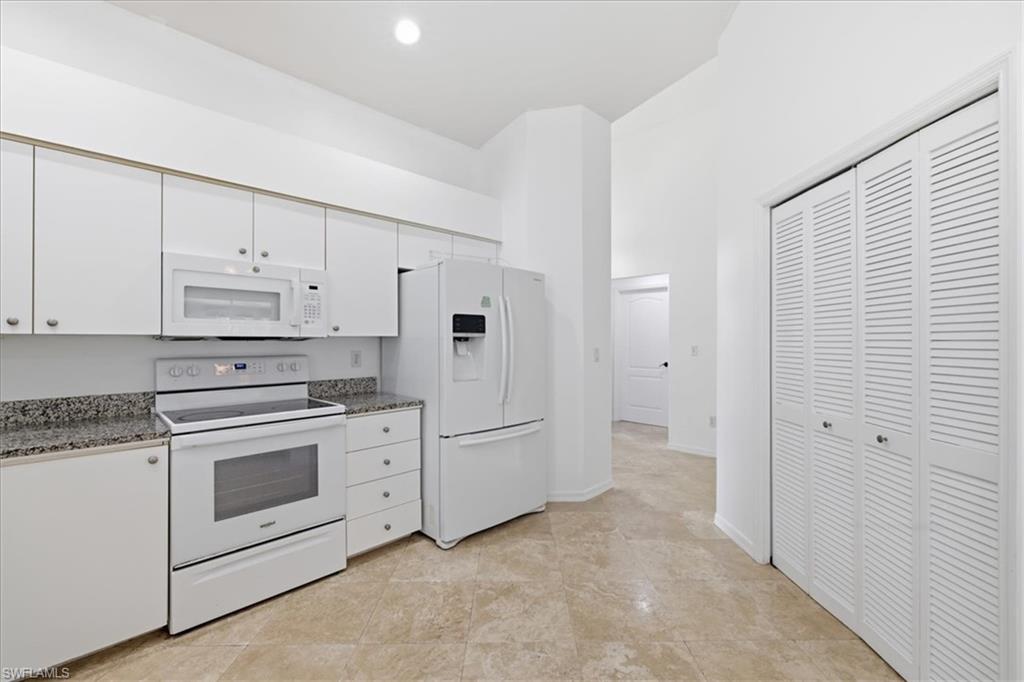 Kitchen featuring white cabinetry with silver hardware, white appliance suite, light-toned granite-style countertops, and neutral tile flooring