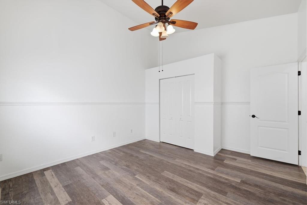 Room featuring a vaulted ceiling with a ceiling fan, wood-finish flooring, white walls, and a bi-fold closet door