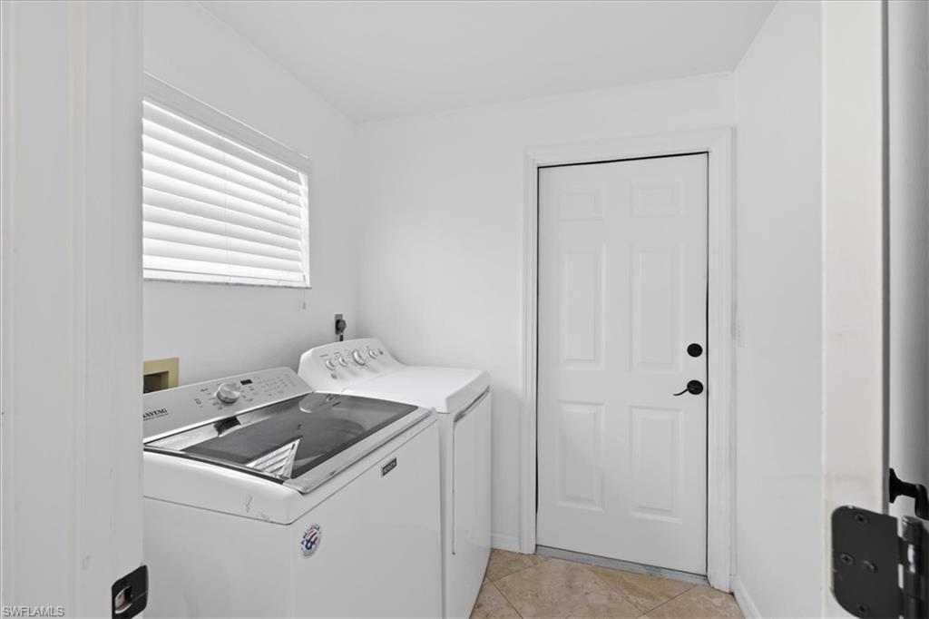 Dedicated utility room featuring a window with horizontal blinds, tiled flooring, and a paneled door with dark hardware