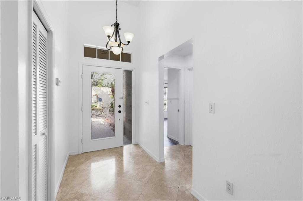Entryway featuring polished tile flooring, a glass-paneled entry door with a transom window, a decorative chandelier, and an adjacent louvered door closet