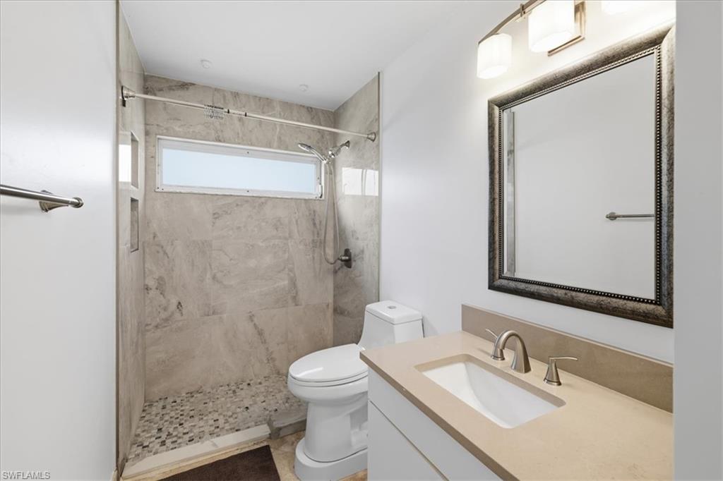 Bathroom featuring a stone-look tiled shower with a pebble floor, horizontal privacy window, a built-in shower niche, and a vanity with an integrated sink and brushed nickel faucet