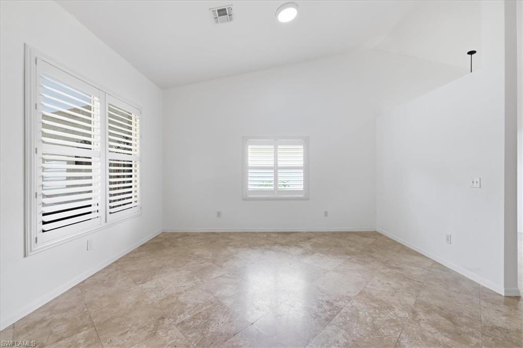 Spacious room featuring vaulted ceilings, a large window with white plantation shutters, a smaller window with white plantation shutters, and light-toned tile flooring