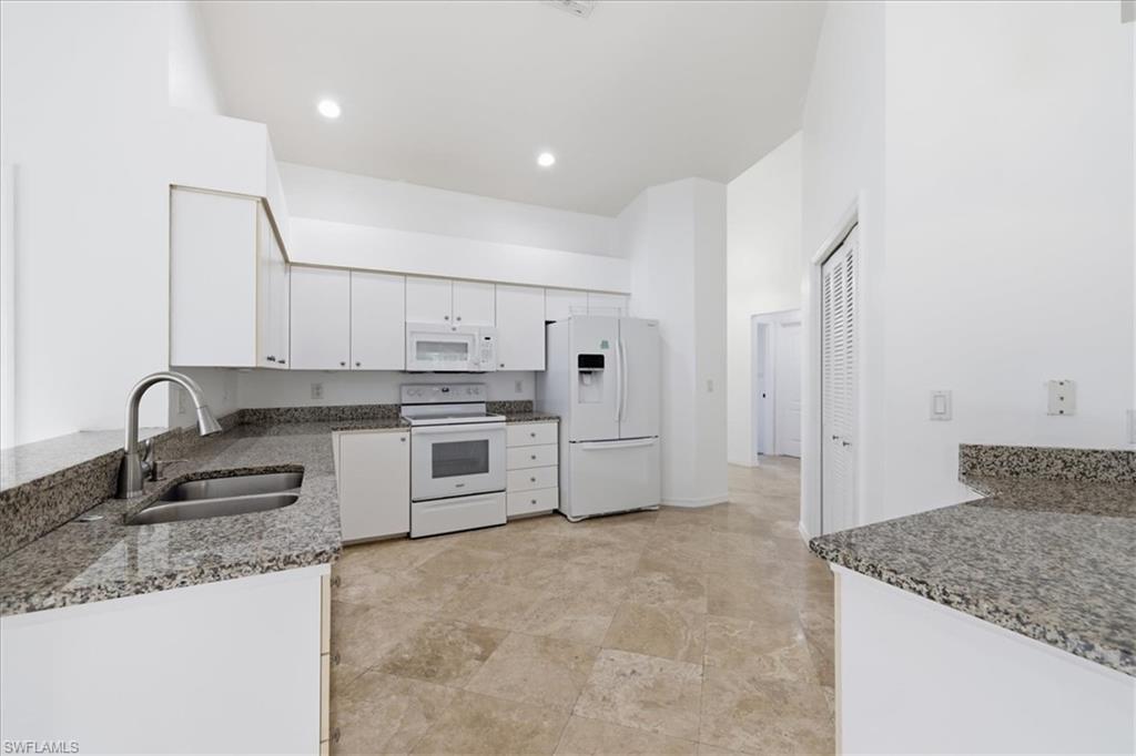 Kitchen featuring granite countertops, white cabinetry, a stainless steel sink with a high-arc faucet, white appliances, and tiled flooring