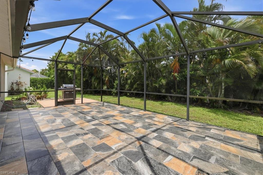 Expansive screened patio featuring multi-toned tile flooring, an outdoor cooking station, and string lighting