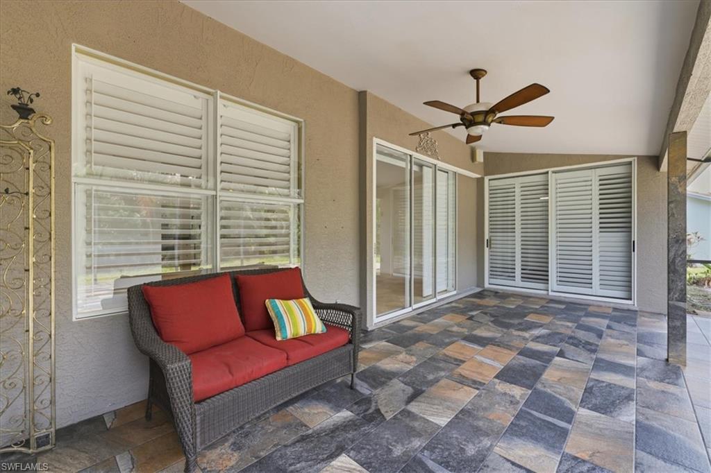 Spacious covered patio featuring multi-toned stone tile flooring, a built-in ceiling fan, and multiple sets of sliding glass doors