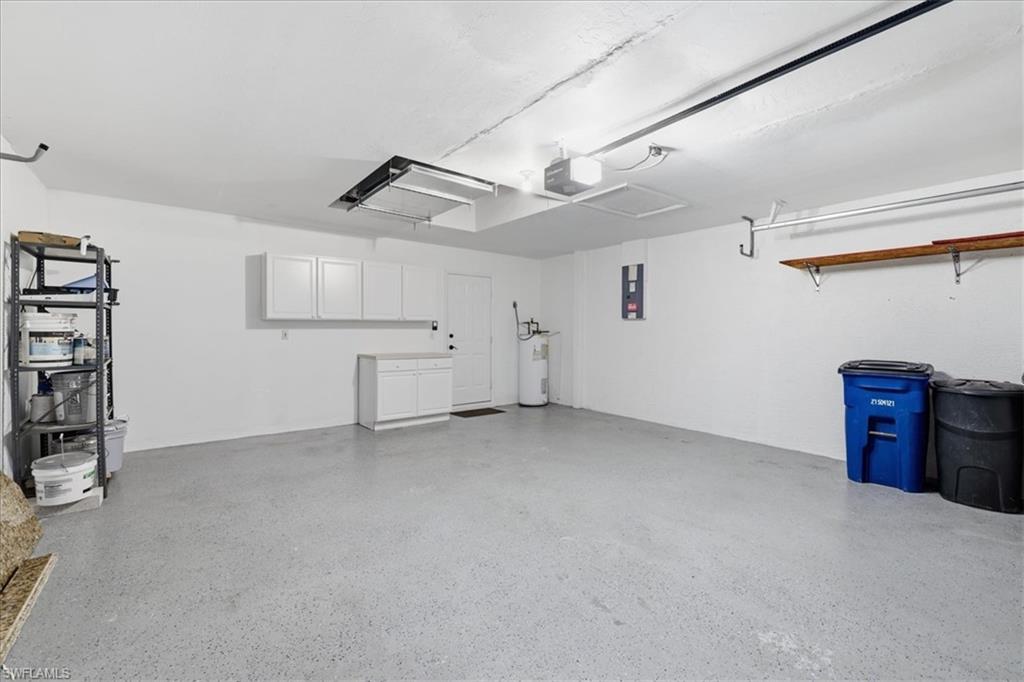 Spacious garage featuring a light gray epoxy floor coating, built-in white cabinetry, a single utility door, and overhead lighting