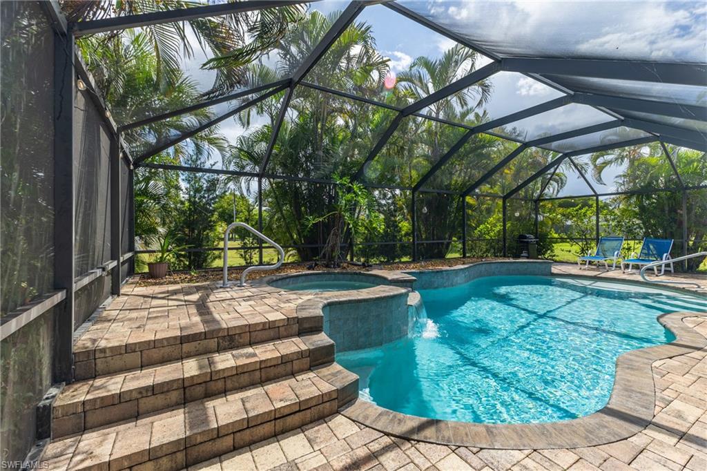 Screened outdoor oasis featuring a freeform swimming pool, integrated spa, and waterfall feature