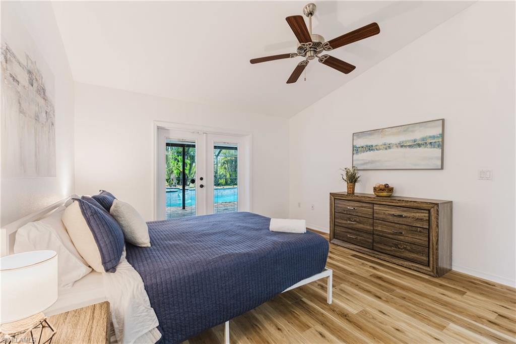 Vaulted ceiling bedroom with light wood-finish flooring and direct access to an outdoor pool area via double French doors