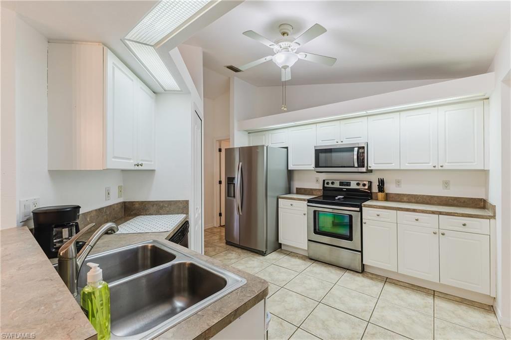 Bright kitchen featuring white cabinetry, stainless steel appliances, a double basin sink, and tile flooring