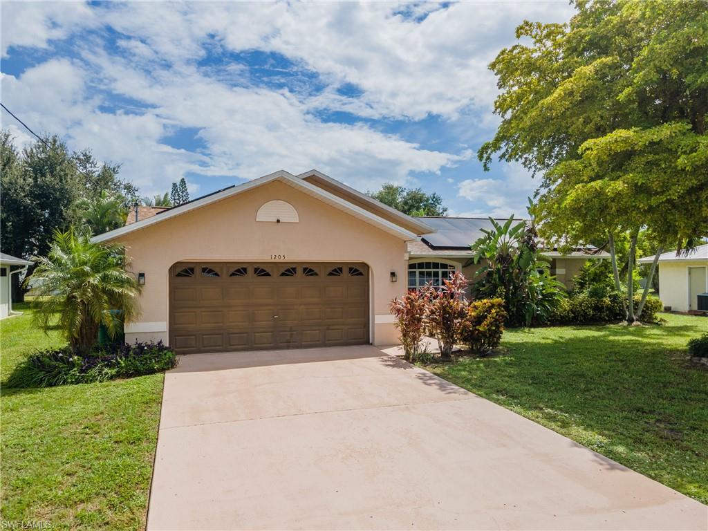 Single-story residence featuring a two-car garage with decorative windows, a paved driveway, and mature landscaping