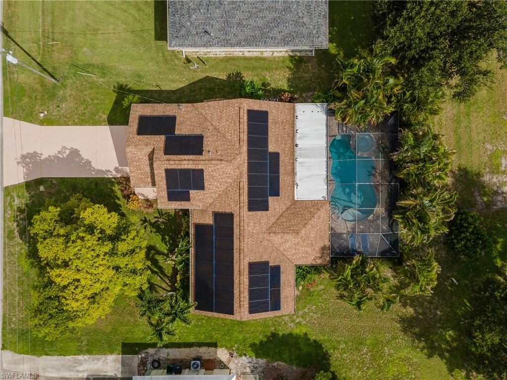 Aerial perspective showcasing a property featuring a pool, screened enclosure, solar panels, mature landscaping, and an extended driveway