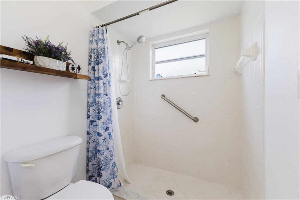 White tiled shower with a window, grab bar, and a single shower head