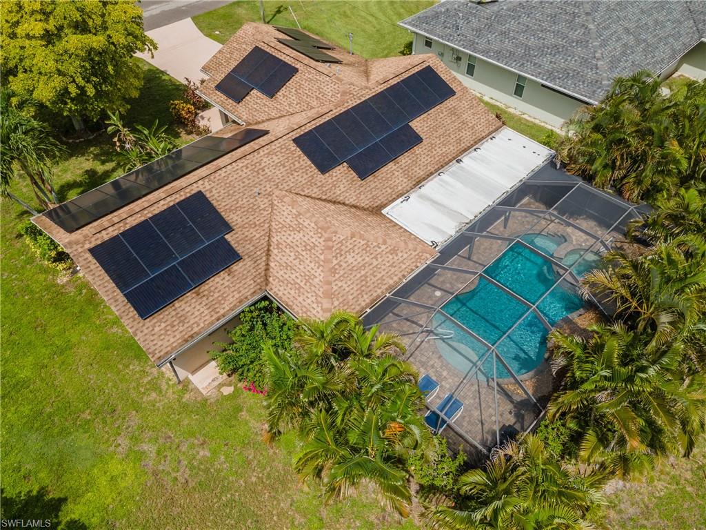 Screened-in pool area featuring a freeform swimming pool with integrated spa, surrounded by paver decking and lush tropical landscaping