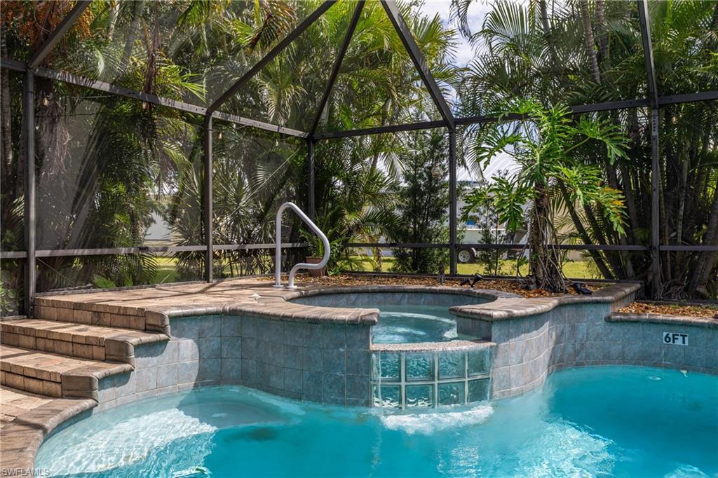 Screened enclosure featuring a swimming pool with integrated spa, tile-lined steps, a water feature with glass block accents, and surrounding tropical plantings