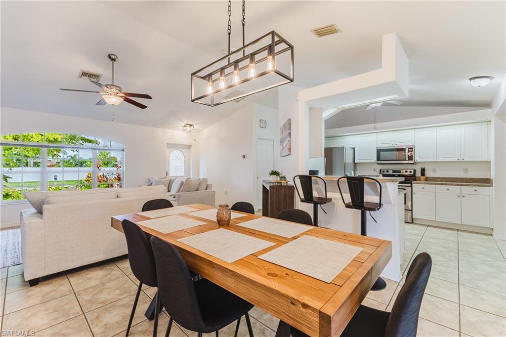 Open-concept living and dining area featuring a wood-finish dining table with seating, tile flooring, and a contemporary linear chandelier