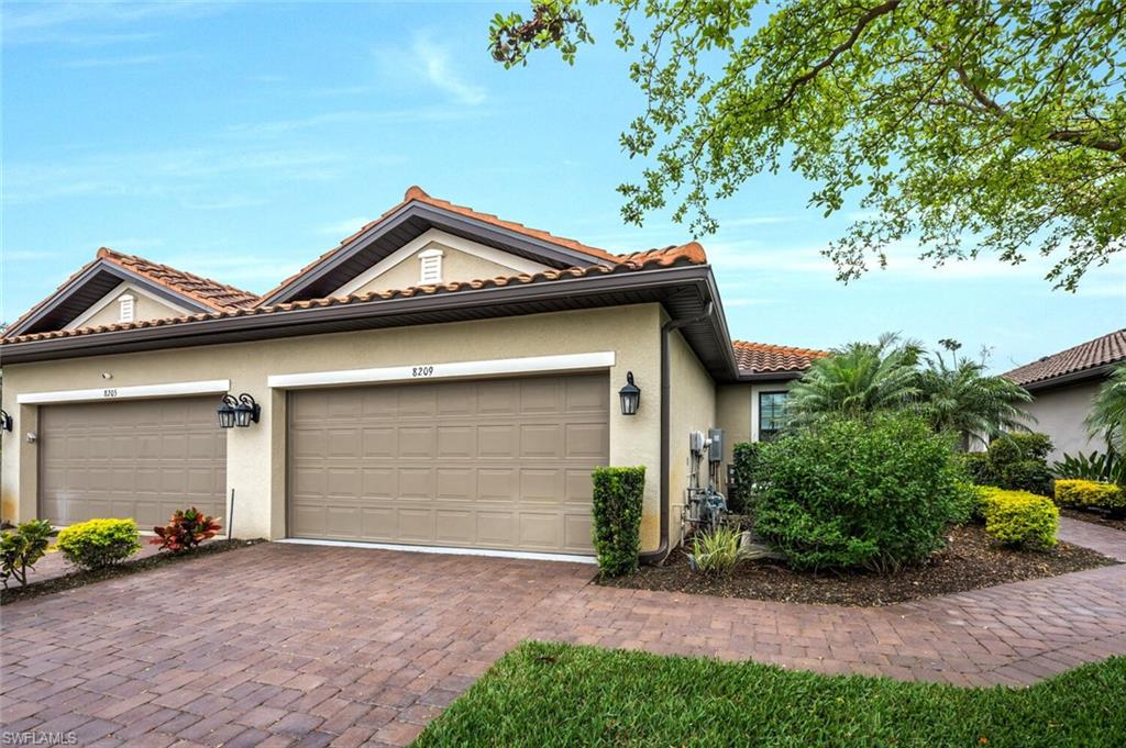 Front exterior featuring a two-car garage with individual doors, a brick paver driveway, and a complementary brick paver walkway