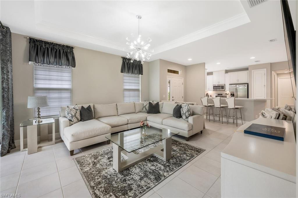 Spacious living area featuring light tile flooring, crown molding, and a contemporary chandelier