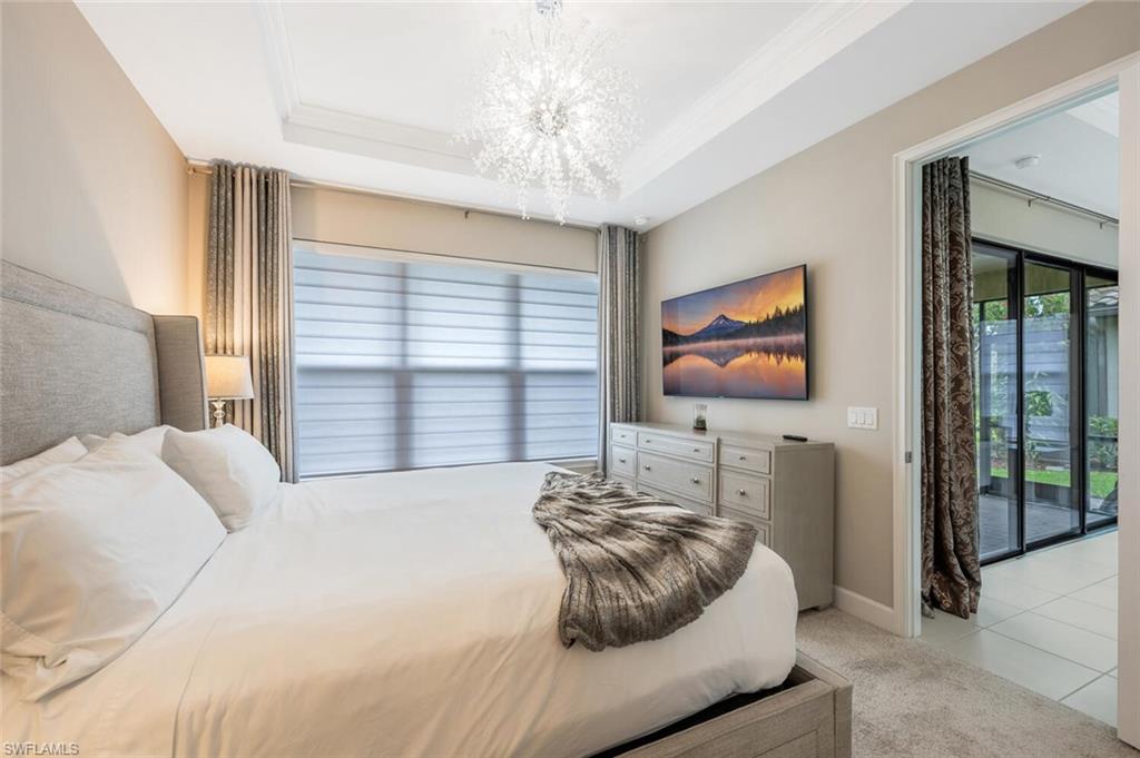 Carpeted room featuring a tray ceiling with a contemporary chandelier, a wide window with horizontal blinds, and direct access to an enclosed patio area with sliding glass doors