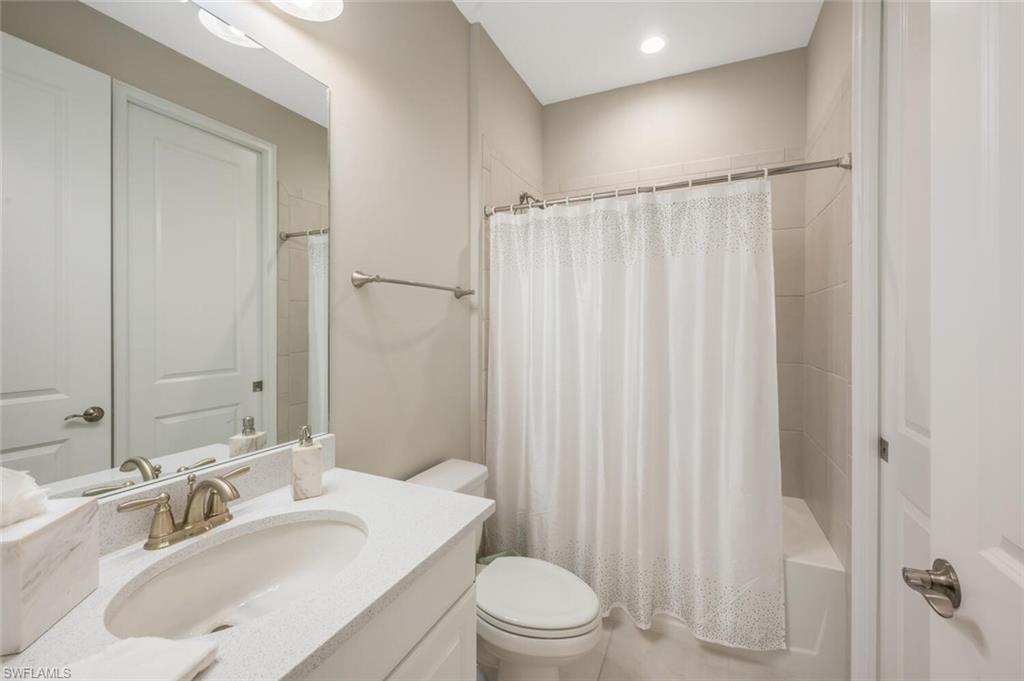 Bathroom featuring a single vanity with an integrated sink and light-colored countertop, brushed gold-tone faucet, and a large wall-mounted mirror
