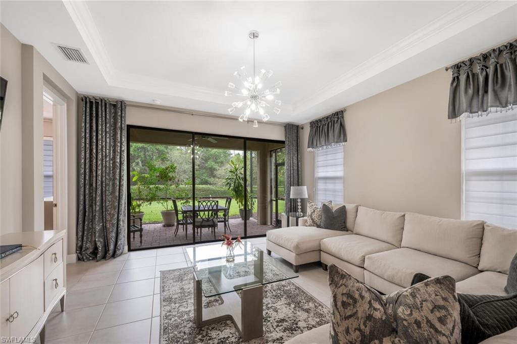 Spacious living area featuring neutral wall tones, tile flooring, a tray ceiling, and a modern chandelier