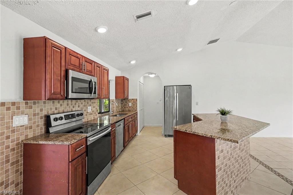 Kitchen featuring wood cabinetry, stainless steel appliances, speckled countertops, a tiled backsplash, and recessed lighting