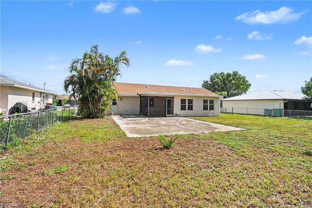 Expansive backyard featuring a concrete patio, screened lanai, mature palm tree, and chain-link fencing