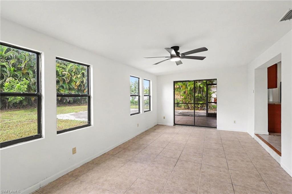 Spacious room featuring tile flooring, multiple windows, a ceiling fan with integrated lighting, and direct access to an outdoor area through sliding glass doors