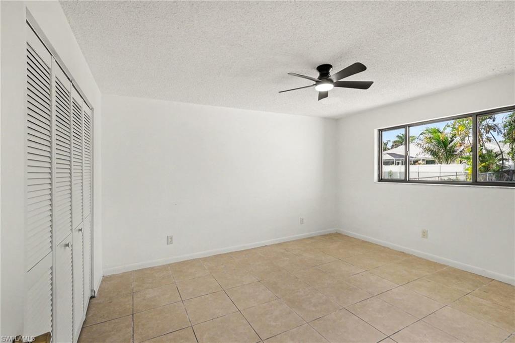 Spacious bedroom with tile flooring, abundant natural light from multi-pane windows, ceiling fan with integrated lighting, and louvered closet doors providing convenient storage solutions