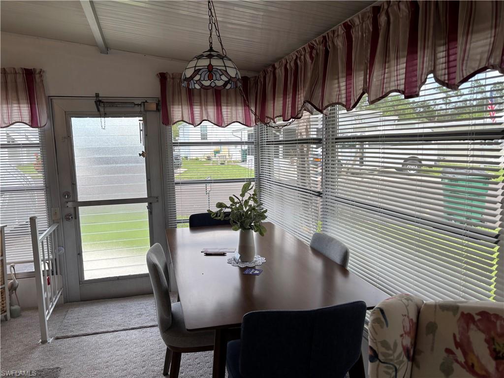 Dining area with a stained-glass style pendant light fixture, multiple windows with blinds, and a glass-paneled exterior door