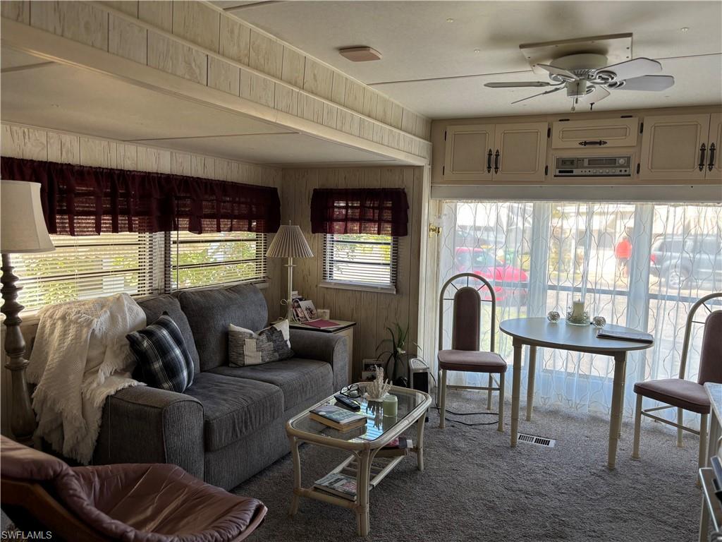 Living room featuring carpet flooring, a ceiling fan, and wooden walls