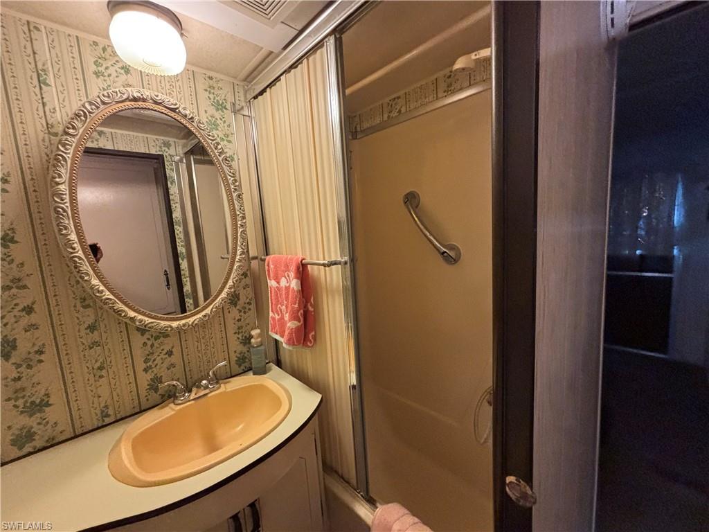 Bathroom featuring a built-in vanity with an integrated sink, an oval wall mirror with an ornate frame, a shower enclosure with sliding doors, and patterned wallpaper