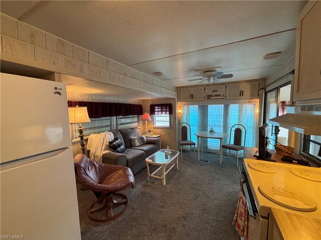Compact living area with carpet flooring, a built-in ceiling fan, and window treatments