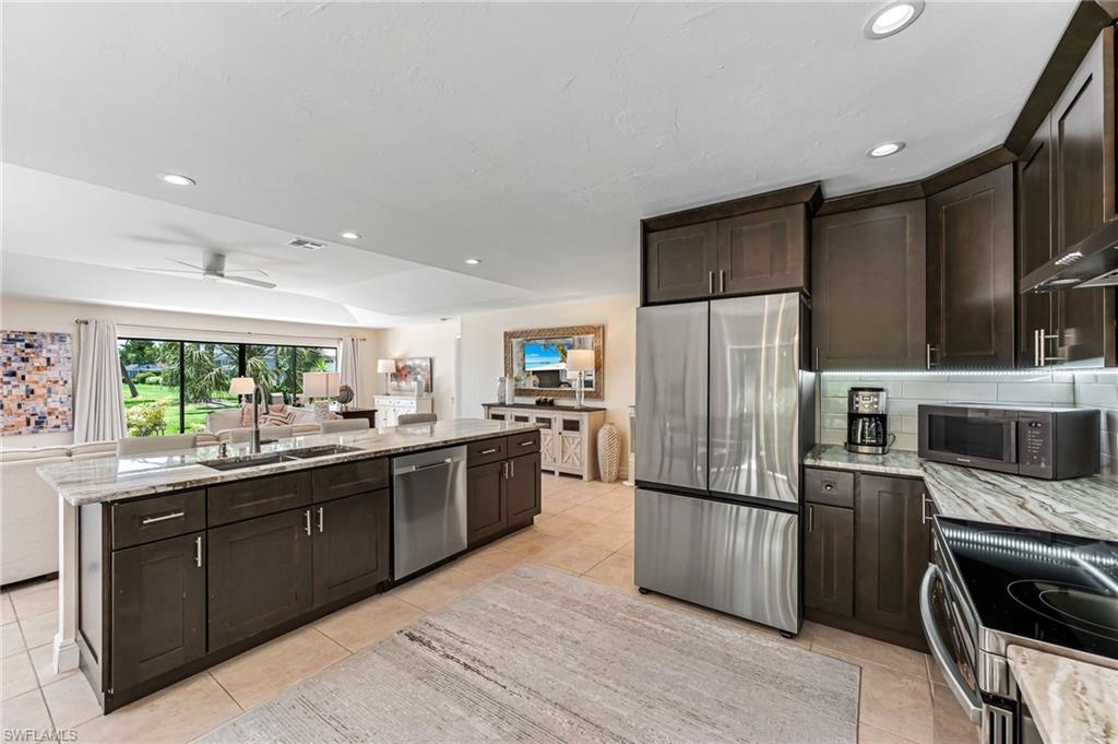 Kitchen featuring appliances with stainless steel finishes, tasteful backsplash, light stone counters, light tile patterned flooring, and ceiling fan