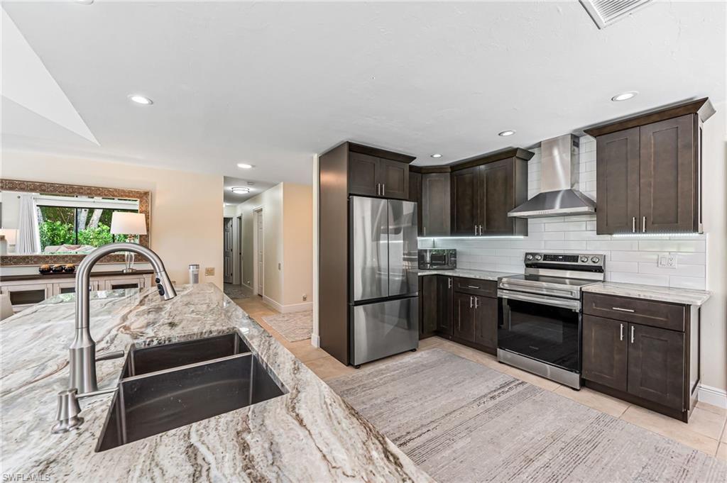 Kitchen with tasteful backsplash, wall chimney range hood, stainless steel appliances, sink with island.