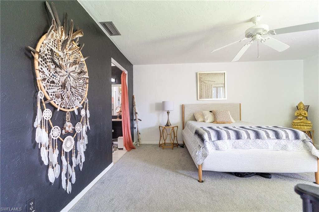 Carpeted bedroom featuring white walls, a ceiling fan with light fixture, and a dark accent wall