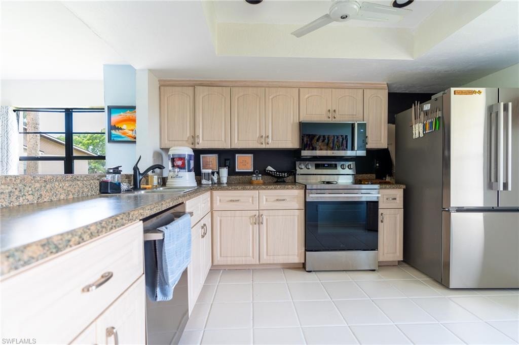 Kitchen featuring light wood-finish cabinetry, stone-finish countertops, stainless steel appliances, and white tile flooring