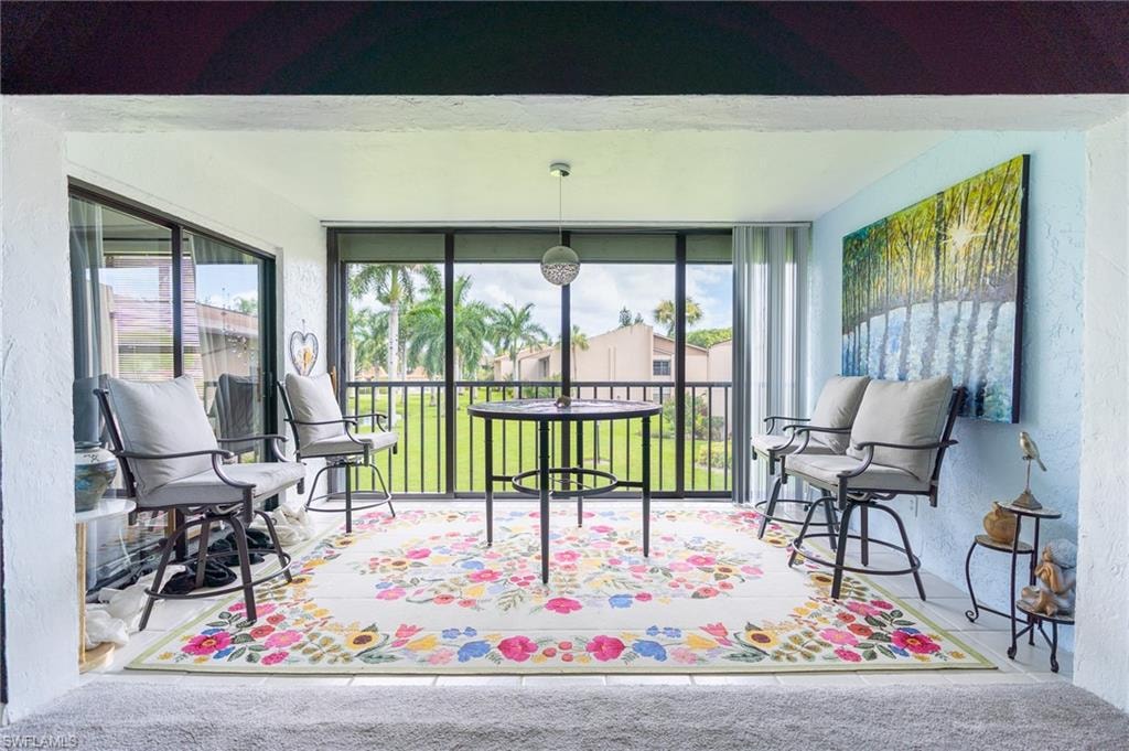 Screened-in lanai featuring a black metal railing, sliding glass doors, white tiled flooring, a light blue accent wall, and an overhead light fixture