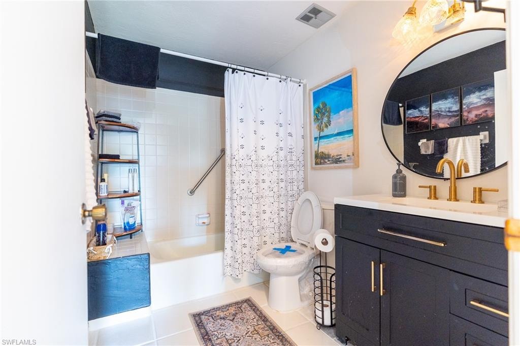 Contemporary bathroom featuring a dark vanity with a white countertop, round black-framed mirror, and brass-finish fixtures
