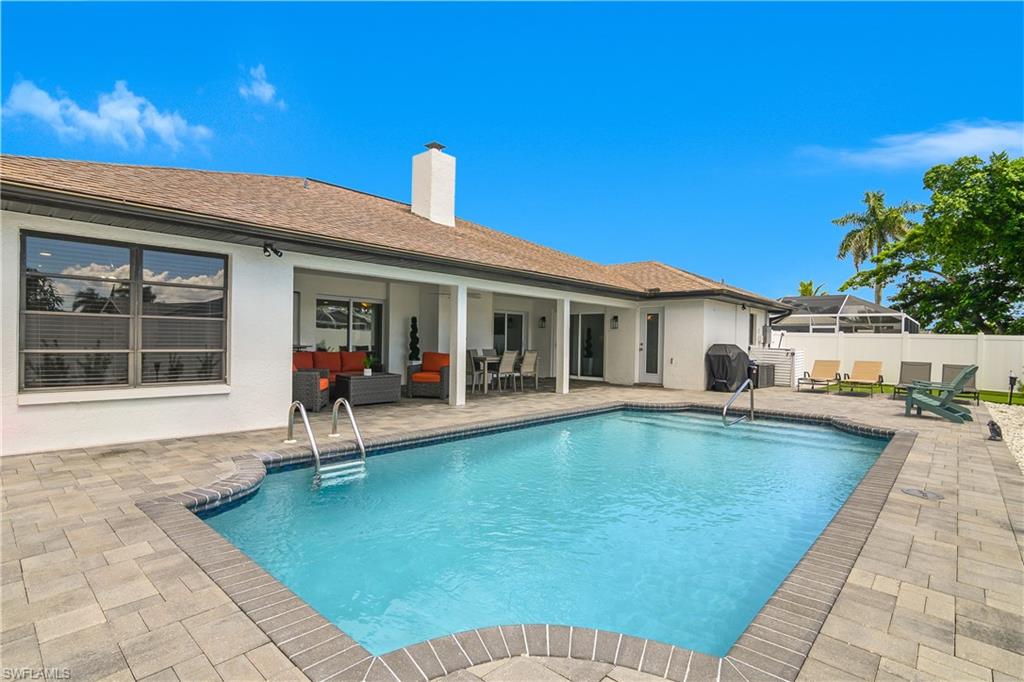 Expansive outdoor living area featuring a rectangular swimming pool with integrated steps, surrounded by a paver patio