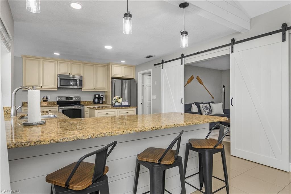 Kitchen featuring light-toned cabinetry, stainless steel appliances, and a granite countertop breakfast bar with pendant lighting