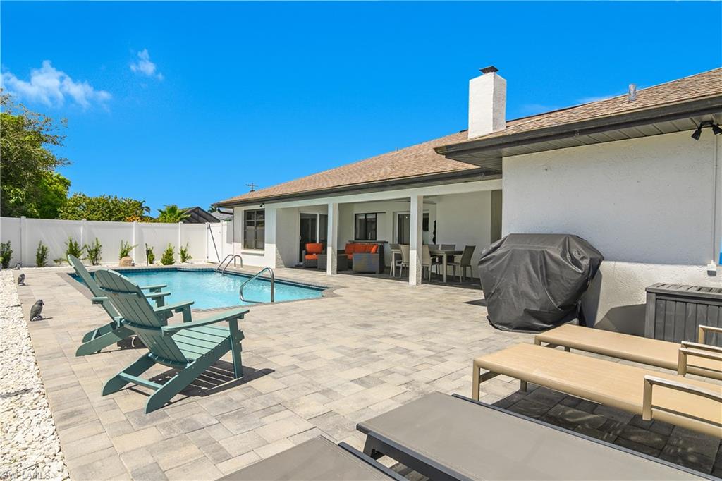 Private backyard featuring a swimming pool, paver patio, covered patio space, and white privacy fencing