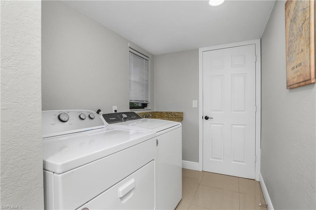 Utility area featuring light gray walls, built-in countertop with a flecked surface, ceramic tile flooring, a window with horizontal blinds, and a paneled door with black hardware