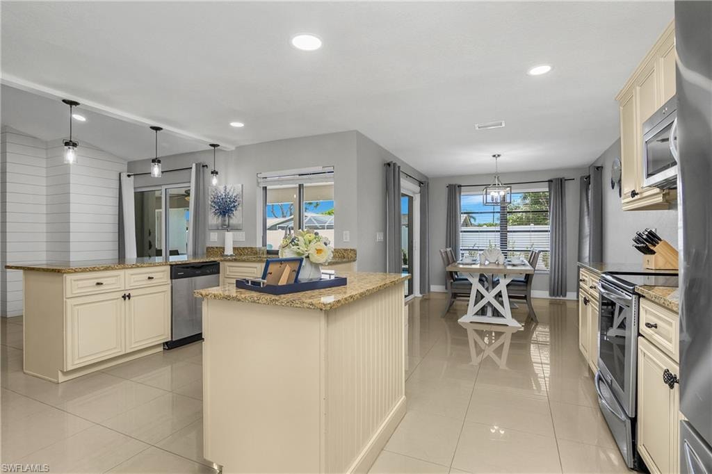 Bright kitchen featuring a double island layout with light-colored cabinetry and stone-finish countertops, stainless steel appliances, and sleek tile flooring