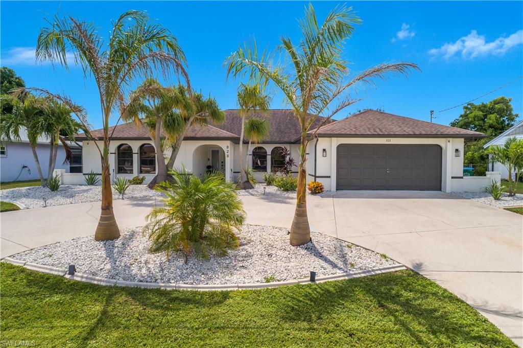 Elegant stucco residence showcasing a circular landscape island with mature palm trees, manicured lawn, and decorative rock hardscaping