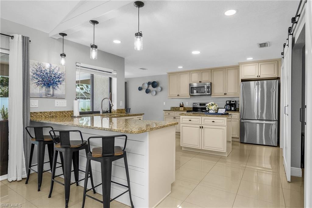 Kitchen featuring a central island, light-toned cabinetry, stainless steel appliances, and granite countertops
