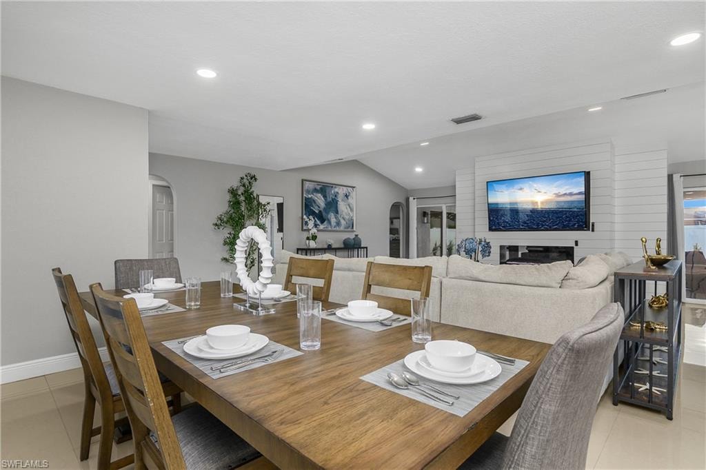 Open-concept dining and living area featuring a wood-finish dining table with seating for six, recessed ceiling lighting, white shiplap accent wall, and a media wall with built-in entertainment cabinetry