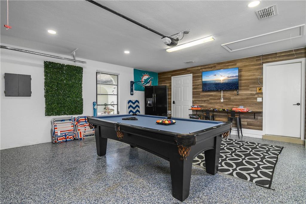 Recreation space featuring textured wood-finish accent wall, durable epoxy flooring, recessed lighting, and a window with horizontal blinds