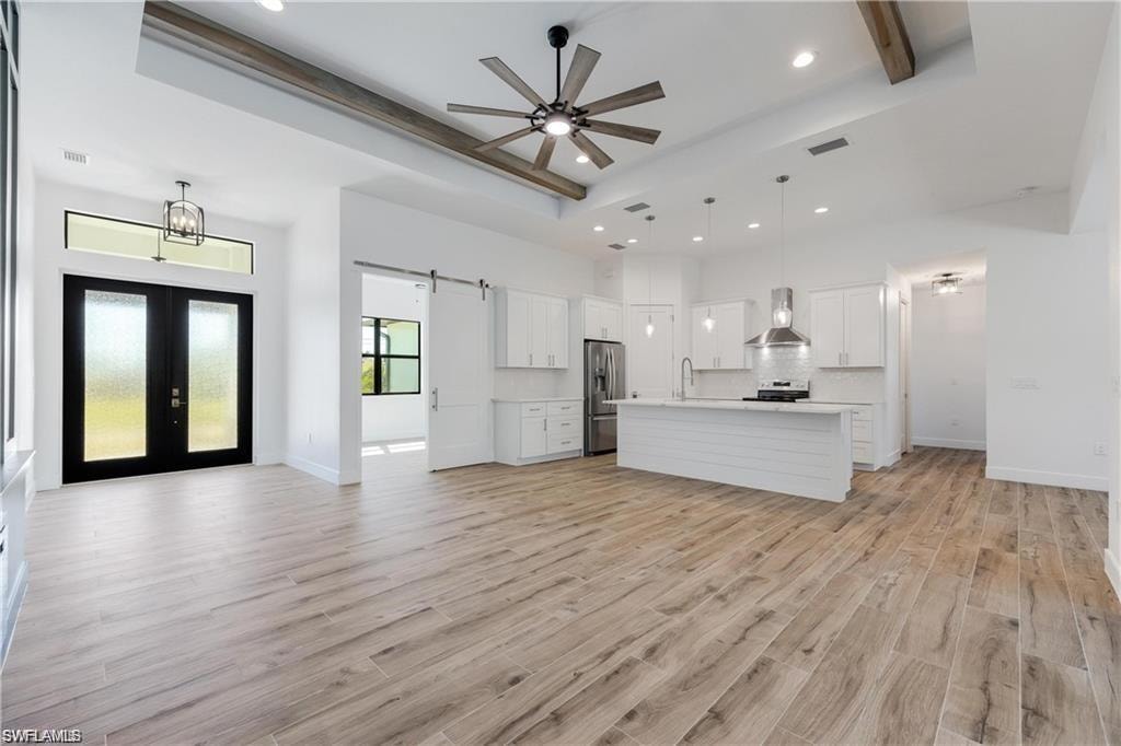 Kitchen featuring appliances with stainless steel finishes, decorative light fixtures, a center island with sink, and wall chimney exhaust hood