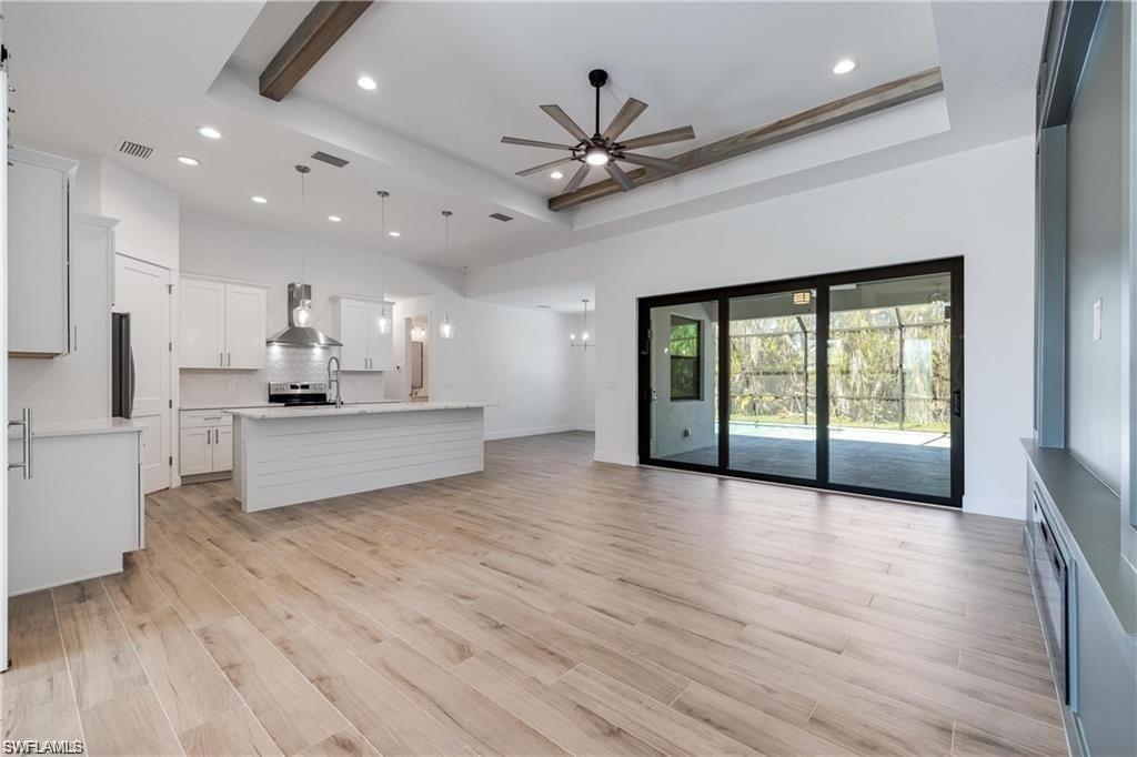 Unfurnished living room featuring a tray ceiling, light hardwood / wood-style floors, ceiling fan, and a towering ceiling