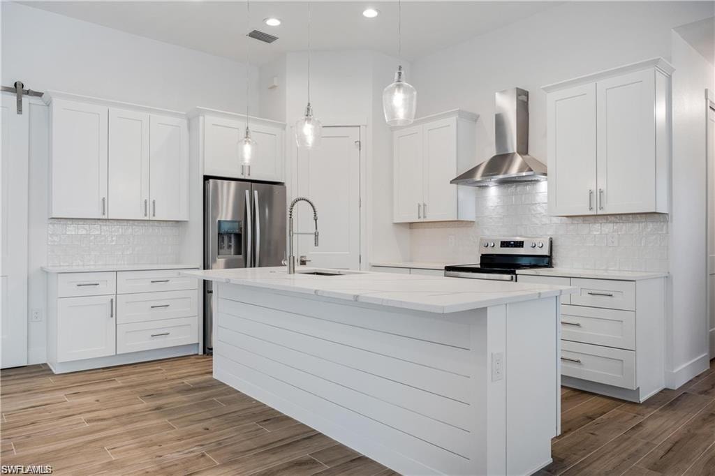 Kitchen with pendant lighting, wall chimney range hood, sink, white cabinetry, and stainless steel appliances